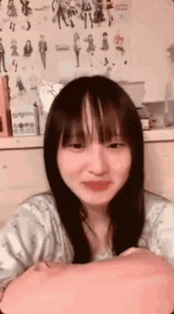 a girl with long black hair and bangs is sitting in front of a wall with drawings of people on it .