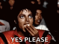 a man in a red jacket is eating popcorn while watching a movie in a theater .
