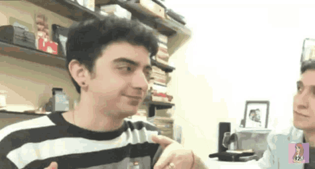 a man in a striped shirt is talking to another man in a room