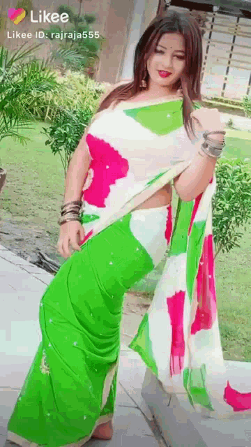 a woman in a green and white saree is standing in a garden .