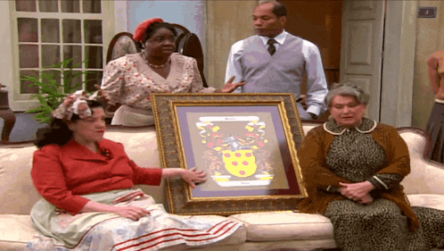 a group of people are sitting on a couch holding a framed picture with a coat of arms on it