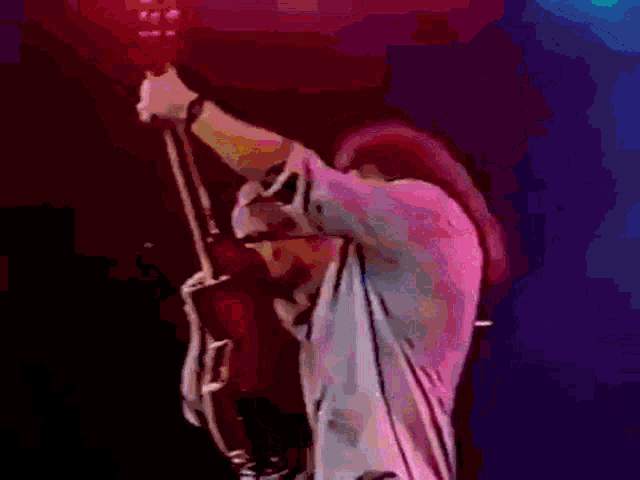 a man is holding a guitar in the air while another man sings into a microphone behind him