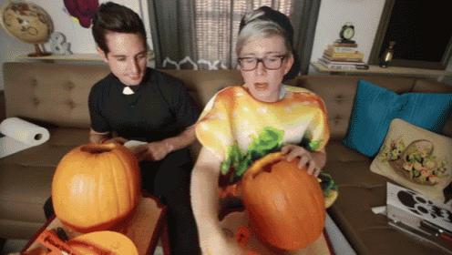 two men are carving pumpkins in a living room and one of them is wearing glasses