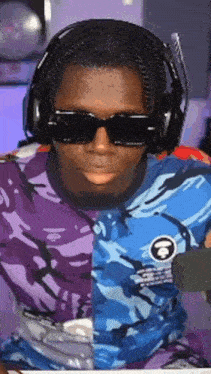 a man wearing headphones and sunglasses is sitting in front of a microphone and making a funny face .