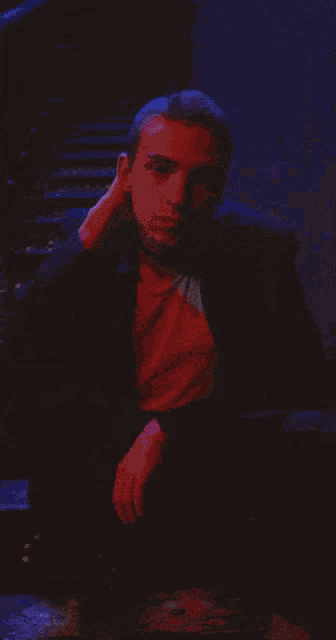 a man in a suit is sitting in a dark room with a blue light behind him