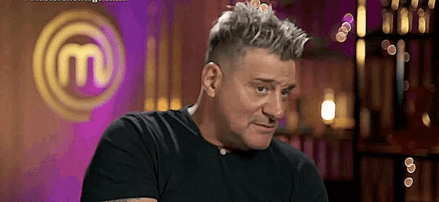 a man in a black shirt is sitting in front of a masterchef logo .
