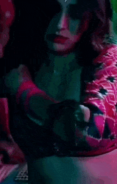a woman in a red top and black bra is sitting on a bed .