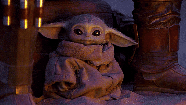 a baby yoda is sitting in the sand with a person standing behind him