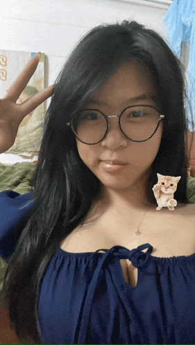 a woman wearing glasses is giving a peace sign with a cat on her shoulder