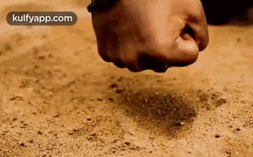 a close up of a person 's fist hitting a pile of dirt on the ground .