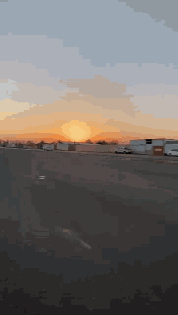 the sun is setting over a parking lot with a lot of cars parked on the side of the road .