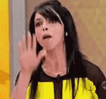 a woman in a yellow and black jacket is making a funny face and waving her hand .