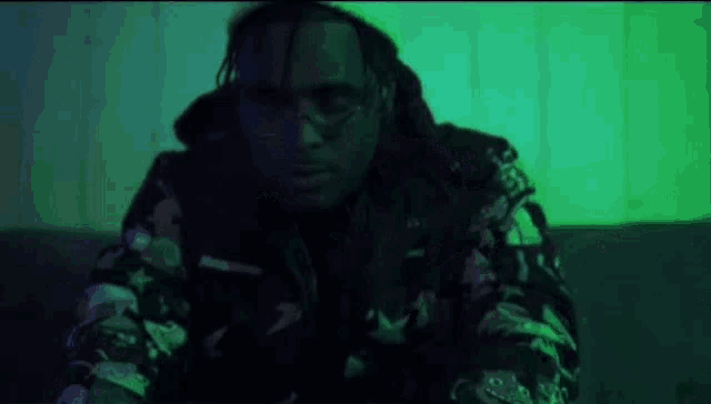 a man with dreadlocks is sitting on a couch in a dark room with green lights behind him .