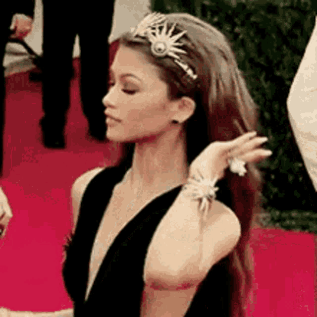 a woman in a black dress is standing on a red carpet with a tiara on her head .