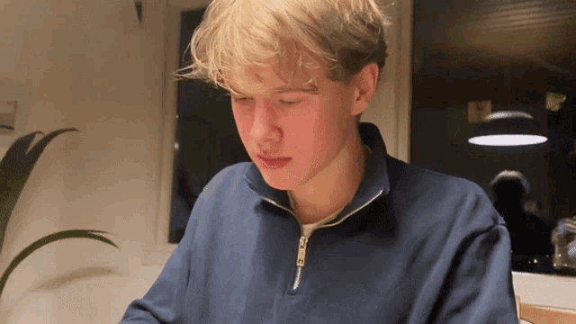 a young man in a blue sweater looks down