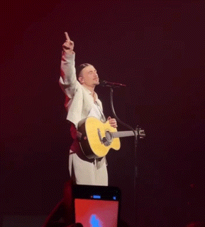 a man singing into a microphone while holding a guitar and giving the middle finger