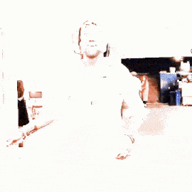 a man with a beard is dancing in a hallway wearing a white shirt and a baseball cap .