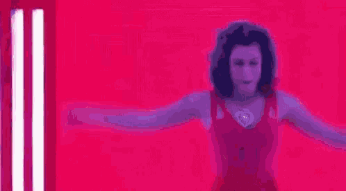 a woman is dancing with her arms outstretched in front of a pink background .