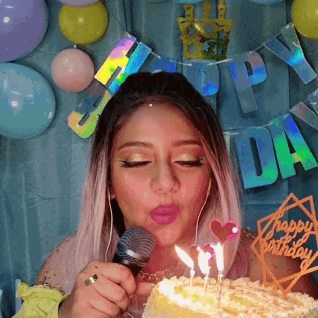 a woman blows out candles on a birthday cake with a happy birthday banner behind her