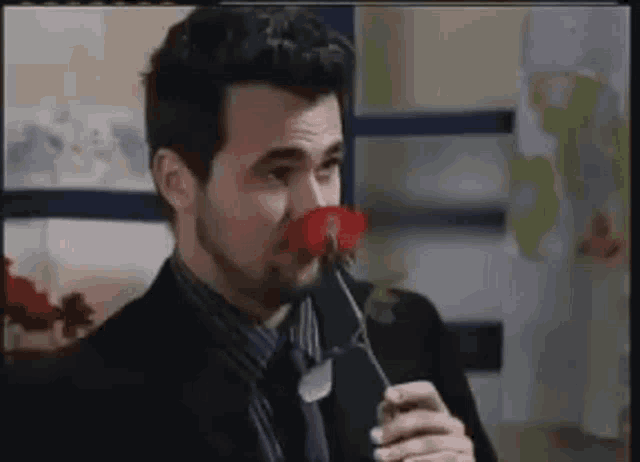 a man in a suit is smelling a red rose on his nose .