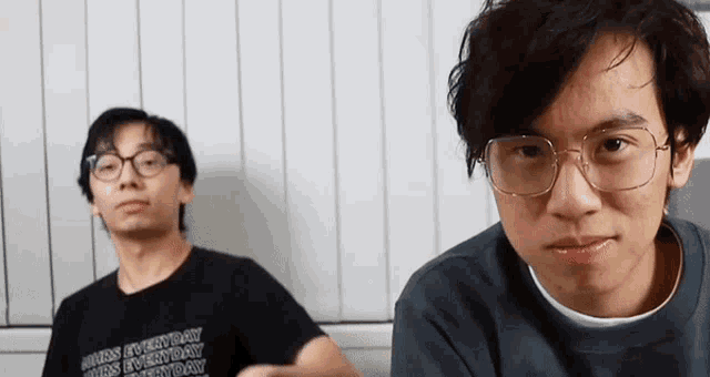two young men wearing glasses and a black shirt are sitting next to each other on a couch .