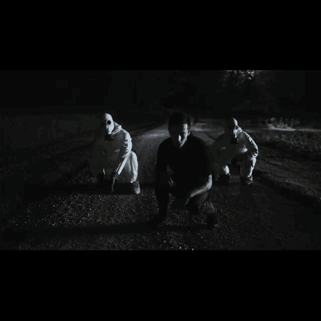 a man in a black shirt is kneeling down next to two men in white hoodies