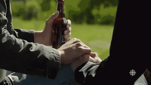 a man is holding another man 's hand while holding a bottle of beer in his hand .