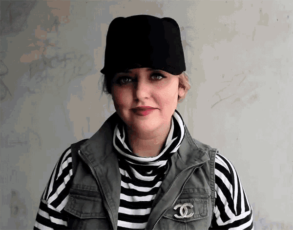 a woman wearing a black hat and a striped shirt has a chanel brooch
