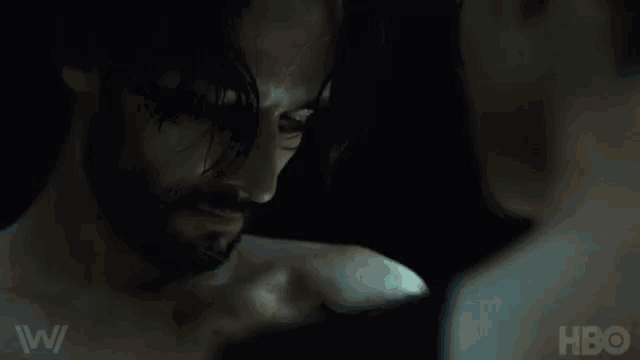 a man with a beard is looking at another man in a dark room with hbo written on the bottom
