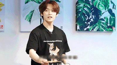 a young man wearing a black t-shirt with a cat on it is standing in front of a wall .