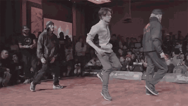 three men are dancing on a stage in front of a crowd that is watching .
