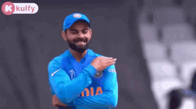a man wearing a blue india jersey is standing with his arms crossed and smiling .