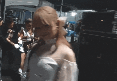 a woman in a white dress stands in a crowd