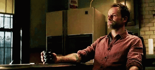 a man in a plaid shirt is sitting at a table with a cup of coffee in his hand .