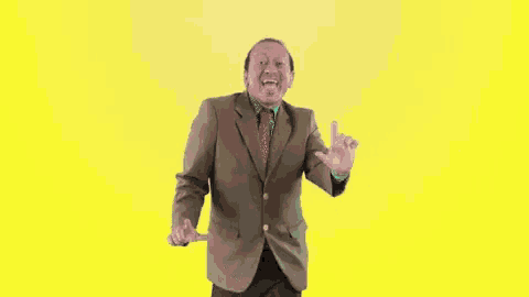 a man in a suit and tie is dancing with his arms outstretched on a yellow background .