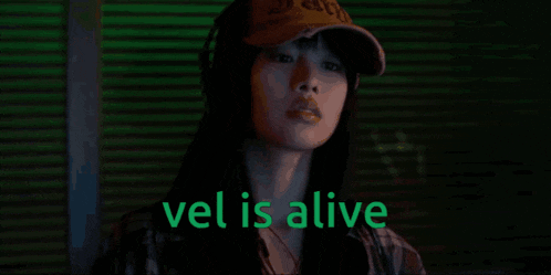 a woman wearing a baseball cap with the words vel is alive above her head
