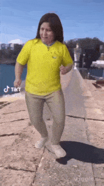a woman in a yellow shirt is dancing in front of a body of water