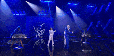a man in a blue suit is dancing on a stage with a woman in white