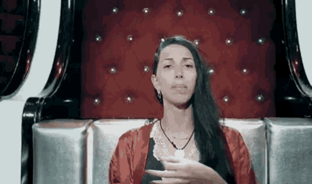 a woman in a red robe is sitting in a chair with her hand on her chin