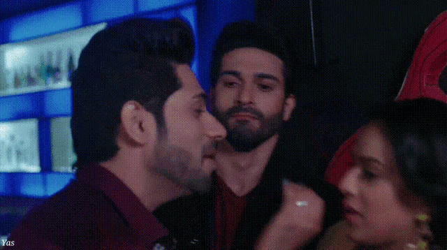 a man with a beard is kissing another man on the cheek in a room .