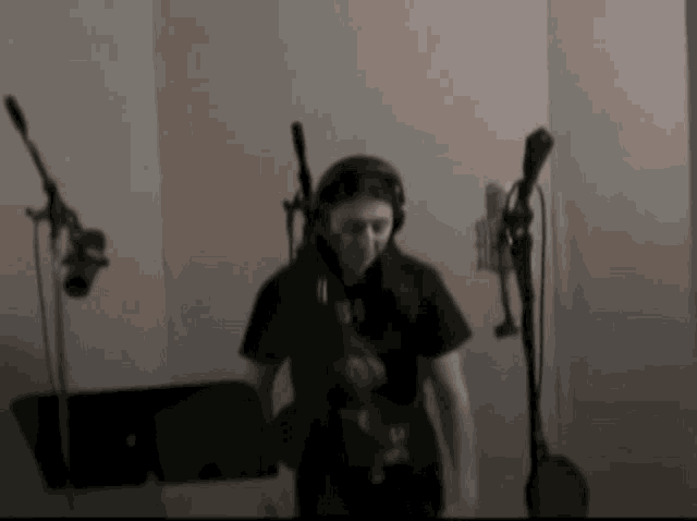 a man wearing headphones and a black shirt is standing in front of a microphone .