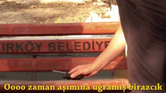 a man is holding a remote control in front of a park bench that says kirkoy belediye