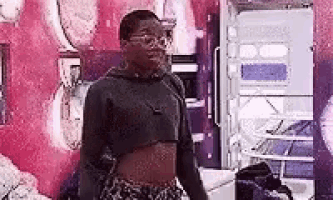 a woman wearing a crop top and glasses is standing in front of a wall .