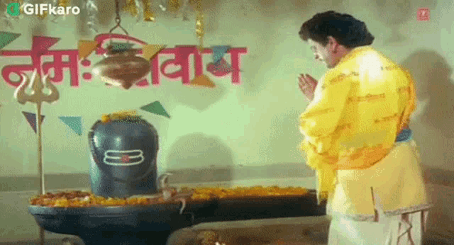 a man in a yellow shirt prays in front of a shiva statue