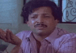 a man with a mustache is sitting at a table with his hands outstretched and making a funny face .