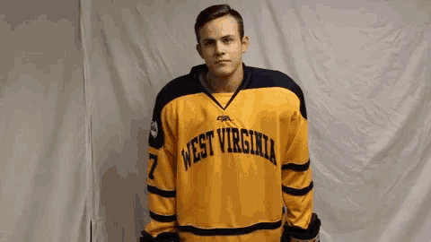 a man wearing a west virginia jersey stands in front of a white wall