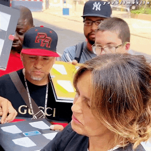a woman wearing a gucci shirt sits in front of a group of people