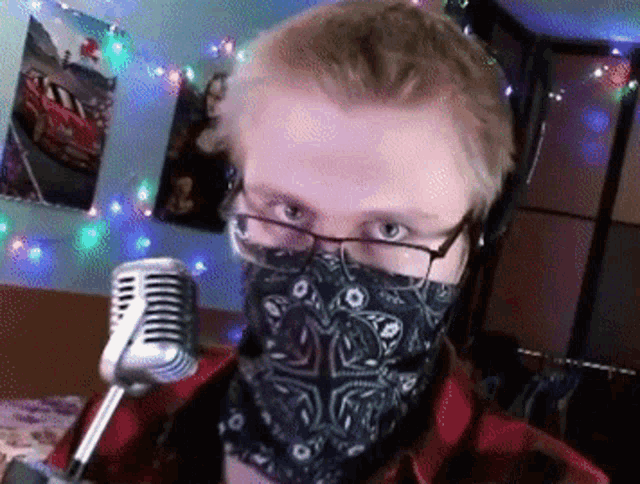 a man wearing glasses and a bandana stands in front of a microphone ..