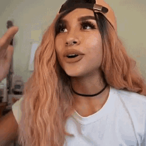 a woman with long blonde hair and a baseball cap is wearing a choker and a white t-shirt .