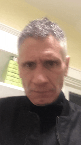 a man with gray hair and a black jacket is looking at the camera